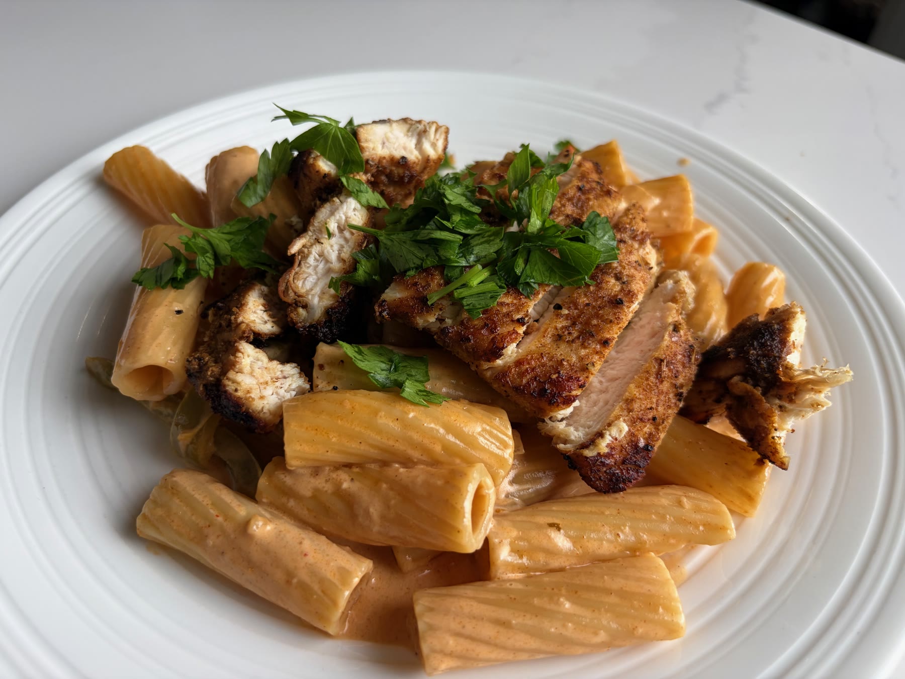 Finished Creamy Cajun Chicken Pasta with rigatoni, blush-orange sauce, sliced Cajun chicken, and parsley